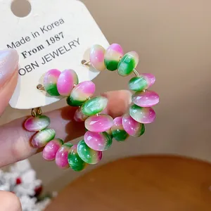 Primer plano de pendientes de aro con cuentas de resina en degradado rosa y verde.