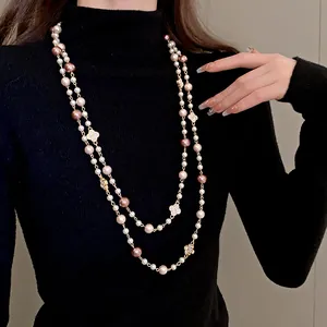 Elegant double-strand pearl necklace with crystal clover accents shown on a black turtleneck.