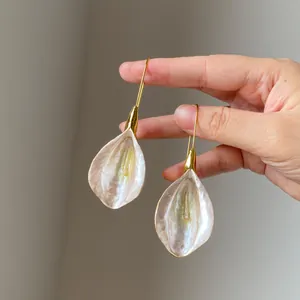 Hand holding vintage pearlescent flower petal dangle earrings with gold hooks