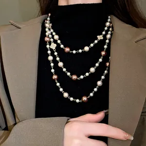 Detail of elegant three-layer long pearl necklace with rhinestone flower charms.