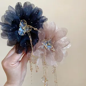 Detail of two elegant chiffon flower hair claws with long tassels held by a hand.