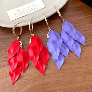 Close-up of matte red and purple leaf tassel earrings with gold hoops on wood background