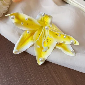 Détail d'une pince à cheveux lys en tissu jaune avec perles blanches sur fond en tissu doux.