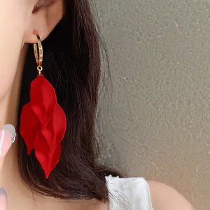 Close-up of vibrant red petal tassel earrings worn by a model against a neutral textured wall.
