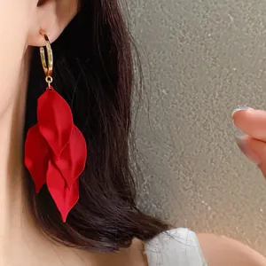 Macro view of elegant red flower petal tassel earrings with gold hoop on model