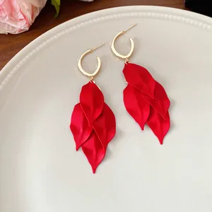 Elegant close-up of red matte petal drop earrings with gold hoop on white ceramic plate