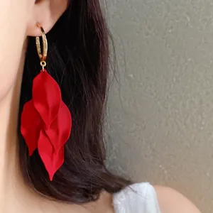 Macro detail of elegant red flower petal tassel earrings with gold hoop worn by a model