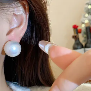 Primo piano di un orecchino a lobo con perla bianca e perno in argento indossato all'orecchio