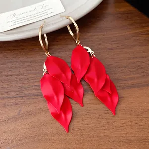 Close-up view of red matte leaf tassel earrings with gold hoops and silver needles.