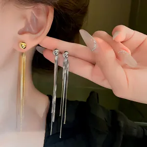 Dettaglio di orecchini a lunga nappa in metallo in oro e argento indossati all'orecchio.