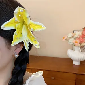 Détail d'une pince à cheveux lys en tissu jaune avec perles sur une coiffure tressée.