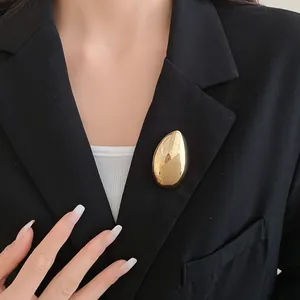 Primo piano di una spilla a goccia d'oro lucido minimalista appuntata su un blazer nero
