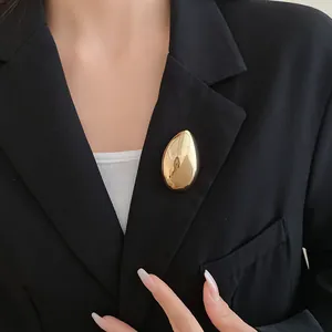 Dettaglio di una spilla minimalista a goccia d'oro su un risvolto di blazer nero elegante