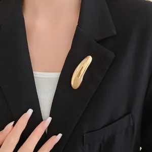 Dettaglio macro di una spilla geometrica in oro lucido sul bavero di un blazer nero.