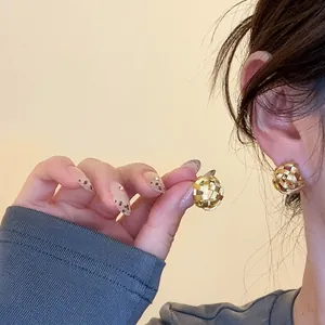 Detail view of gold woven sphere earrings with 18k gold plating on a model