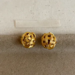 Detailed view of 18k gold-plated woven hollow sphere earrings on a textured background.