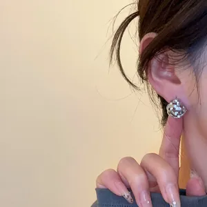 Detail shot of an elegant 18k gold plated woven hollow ball earring worn on an ear