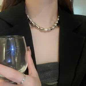Detail of a minimalist silver beaded necklace with a central pearl worn by a stylish model.