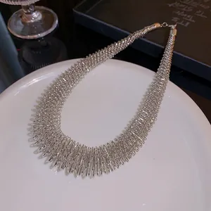 Close-up detail of a minimalist silver spring-textured choker necklace on a plate.