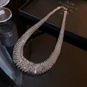 Close-up of a silver spring-textured metal choker necklace on a reflective black surface