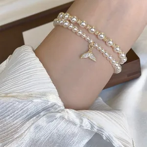 Double-layered pearl bracelet with a sparkling zircon fishtail charm worn on a wrist.