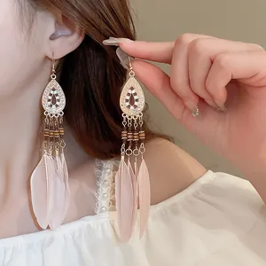 Close-up of bohemian long feather drop earrings with pink feathers and gold detailing.