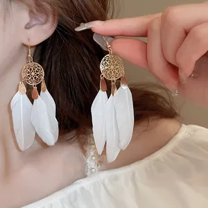 Detailed close-up view of bohemian style white feather tassel earrings with gold accents