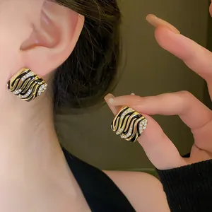 Detail view of square gold stud earrings with black enamel wavy pattern and rhinestones