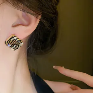 Close-up of square black and gold enamel earrings with crystal accents on a model.