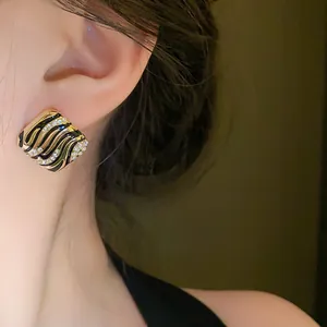 Close-up detail of luxury square black enamel earring with wavy rhinestone accents on ear