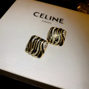 Macro detail of luxury square gold and black zebra pattern earrings with rhinestones.