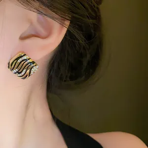 Close-up of square gold and black enamel earrings with crystals on an ear
