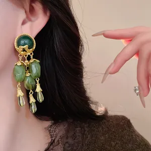 Primo piano di orecchini vintage con nappe verde oliva sull'orecchio di una modella.
