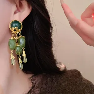 Dettaglio macro di orecchini vintage con nappe verde oliva e accenti in metallo color oro