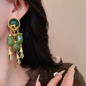 Primo piano di orecchini vintage con nappe verde oliva e accenti dorati su una modella.
