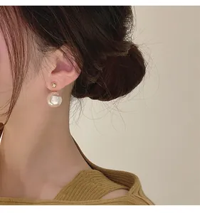 Detailansicht eines eleganten, minimalistischen, vergoldeten Perlenohrrings am Ohr.