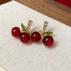 Close-up view of elegant red resin cherry stud earrings with zircon-encrusted stems