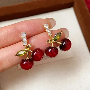 Macro detail of cherry earrings with red resin and sparkling green zircon leaves.