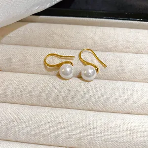 Elegant gold-tone pearl drop earrings with round white pearls on a textured display