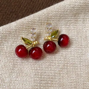 Close-up detail of red resin cherry stud earrings with sparkling zircon leaves.