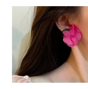 Detail view of a large vibrant pink fabric flower earring worn by a female model