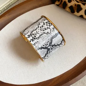 Detailansicht eines breiten Armreifs mit Schlangenmuster und eleganten goldenen Metallkanten.