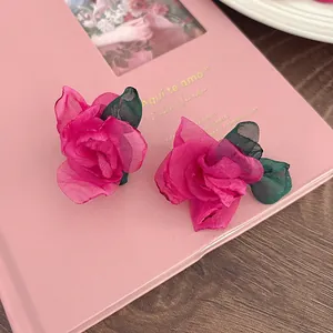 Close-up of pink organza rose stud earrings with green leaves on pink background