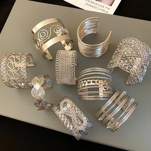 Detailed view of multiple silver metallic cuff bracelets with hollow woven and swirl patterns