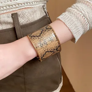 Detailansicht eines breiten Armreifs mit Schlangenmuster und goldfarbenen Rändern am Handgelenk