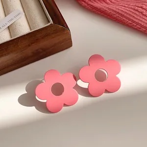 Detailed macro view of vibrant pink matte flower-shaped stud earrings in warm sunlight