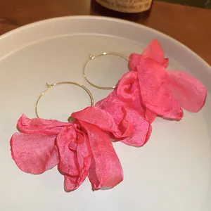 Macro detail of large pink fabric flower petal hoop earrings on a minimalist plate