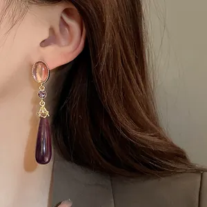 Close-up of vintage court style drop earrings with purple rhinestones on a model.