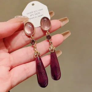 Close-up detail of vintage style purple teardrop dangle earrings with gold metalwork accents
