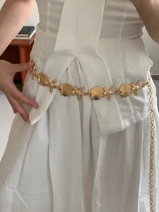 Close-up of gold bohemian waist chain with starfish and shell details on white dress.